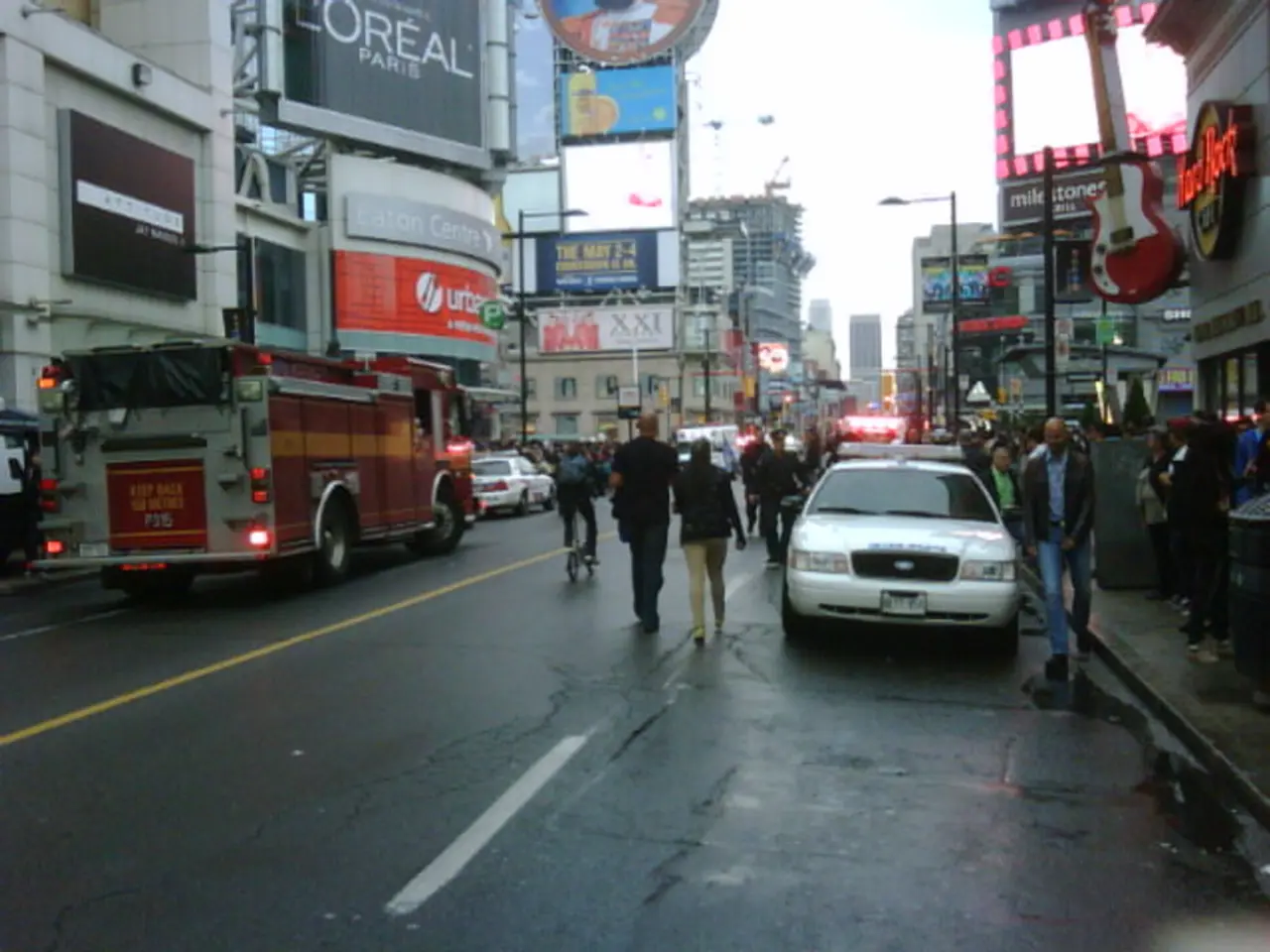 In this image there is a road, on either side of the vehicles are parked to a side, people are...