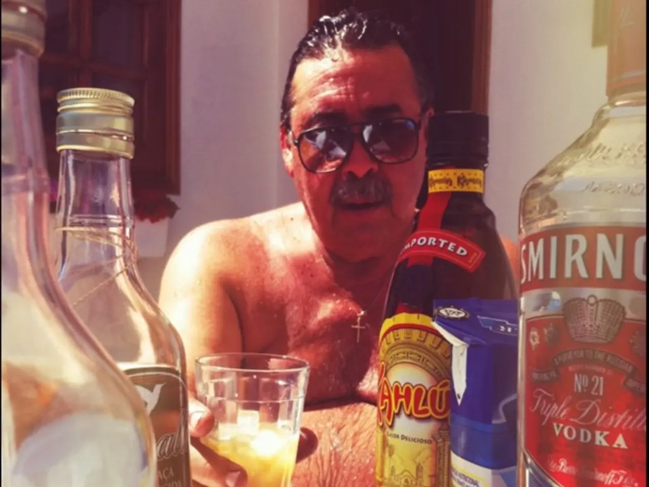 In this image a man is holding a glass with a drink in it and is seeing at the glass wearing a...