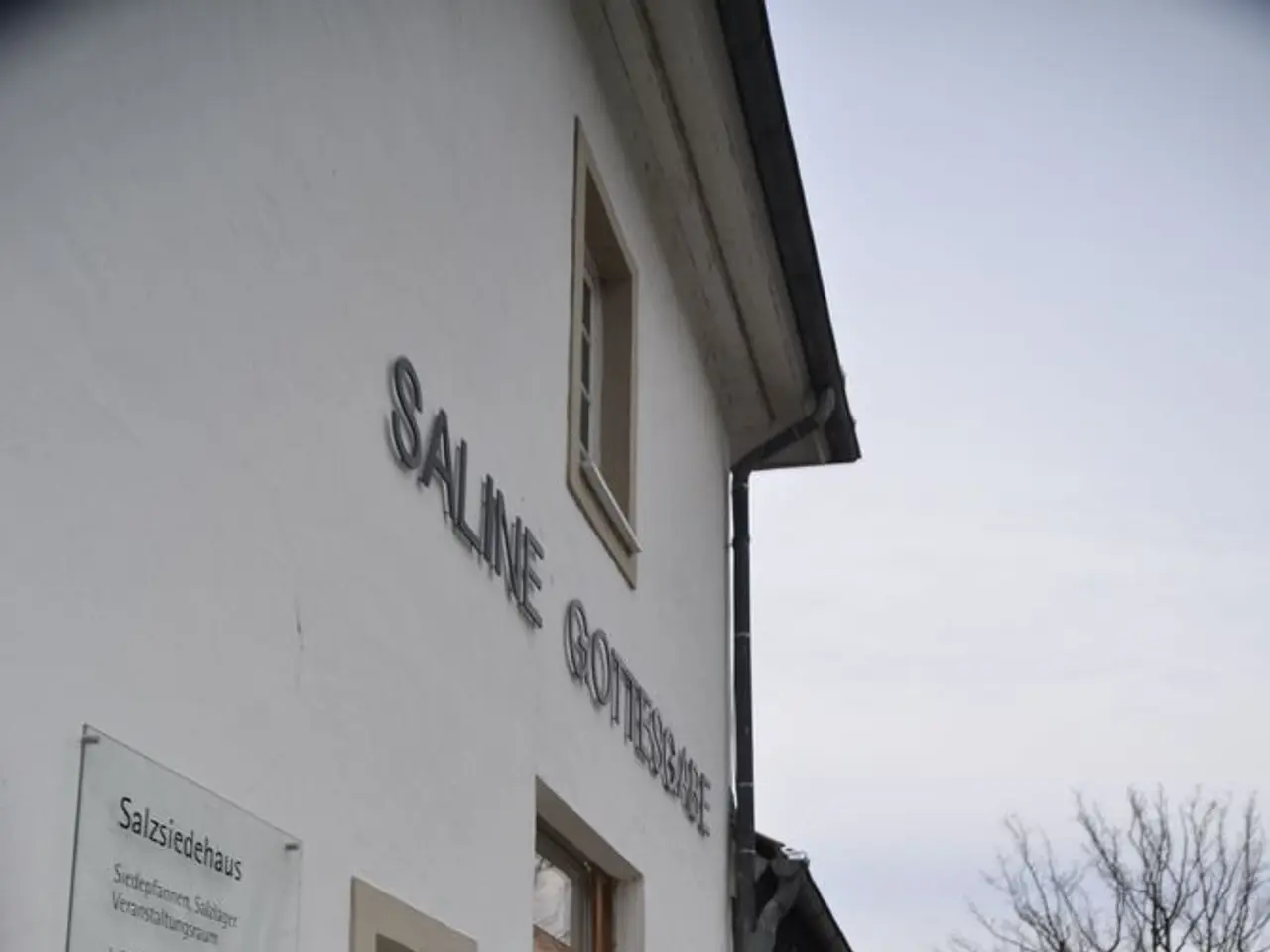 In this image, on the left there is a building on that there are windows, text, glass boards. In...