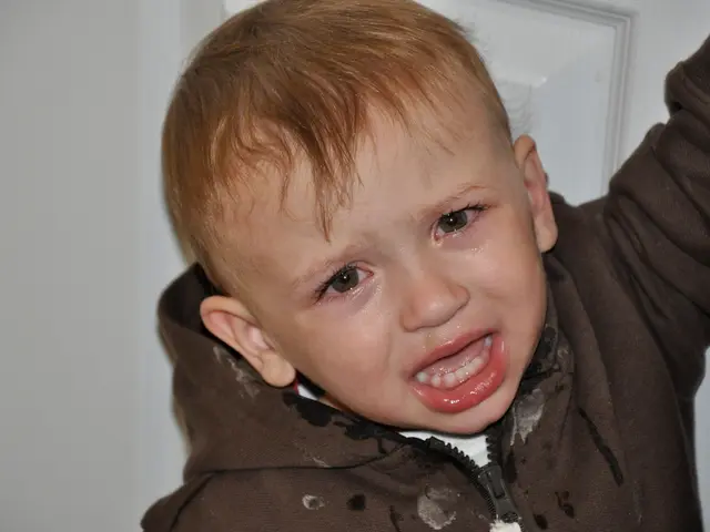 This image consist of a small boy crying is wearing a jacket. In the background, there is a door...