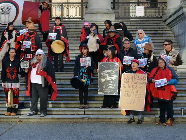 These persons are standing on a steps and holding posters. This man is holding a speaker. Far there...