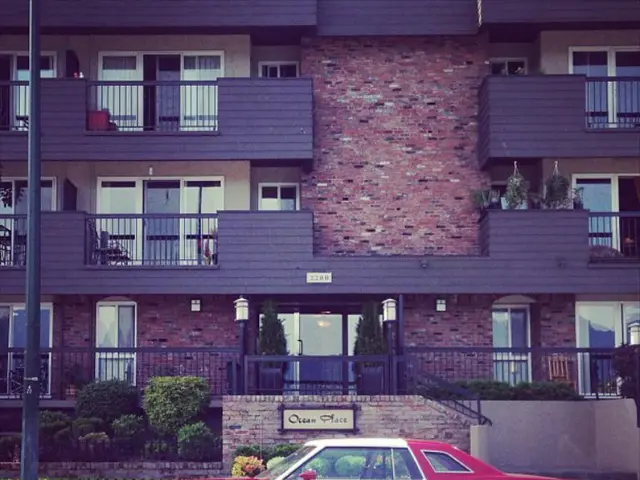 In this picture there is a red color car at the bottom side of the image and there is a building in...