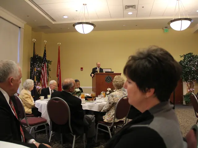 In this image I see few people who are sitting on the chairs and there is a table in front of them...