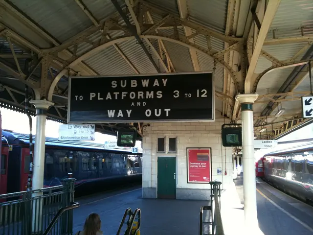 In this image two trains are beside the platform. Two screens are hanged from the roof. Bottom of...