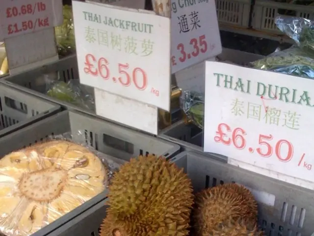 In this image there are fruits in trays and there are price boards.