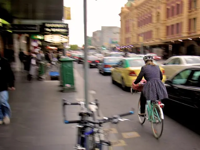 This is a street view. A girl wearing a helmet is riding a cycle on the road. Also there are many...